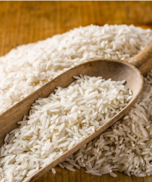 Long-grain white rice in a wooden scoop placed on a pile of rice on a wooden surface.