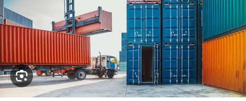 Red shipping container placed in a cargo yard with stacked freight containers in the background.